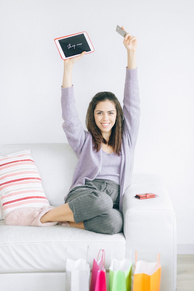 Happy woman enjoying online shopping with tablet and card, surrounded by shopping bags.